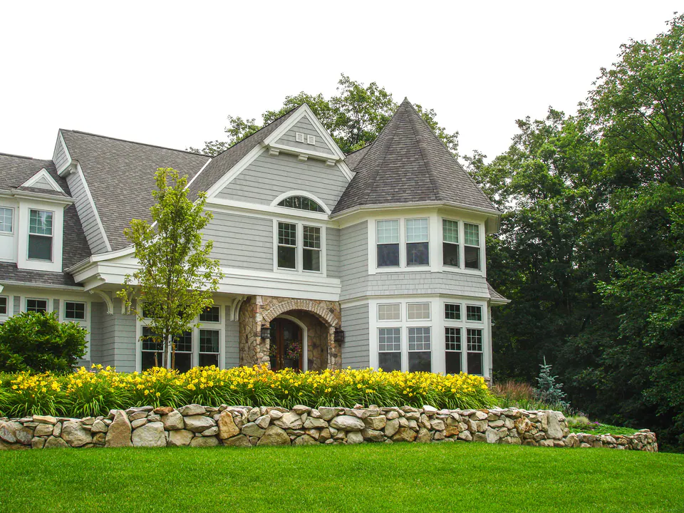 Natural stone garden wall with layered shrubs, perennials, groundcover, and poolside landscape depth
